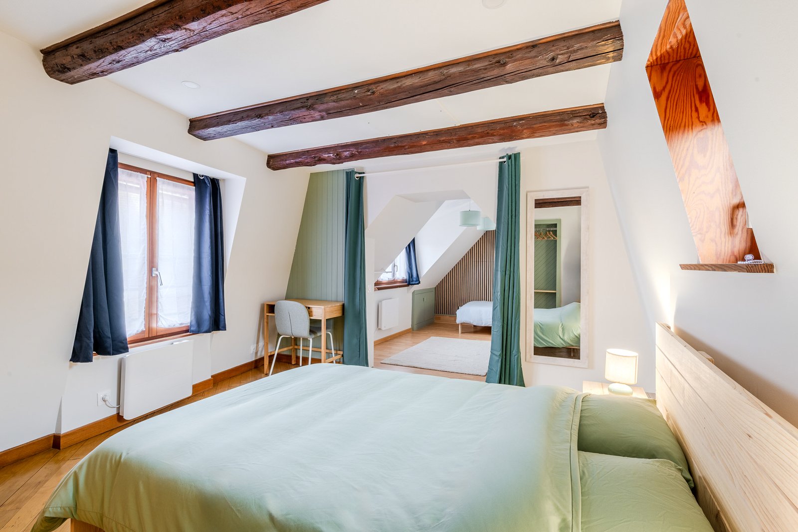 Chambre avec lit double, poutres apparentes et vue vers la seconde chambre